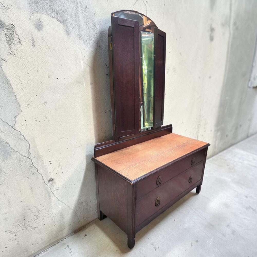 A dark oak dressing chest featuring two wide drawers, a natural wood top surface, and an attached folding triple mirror.