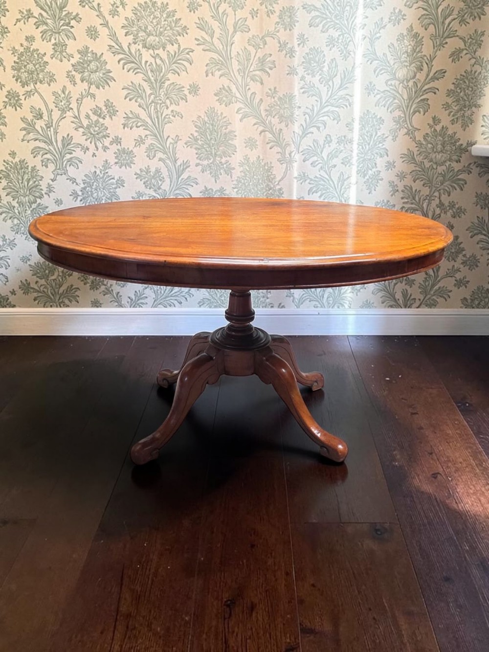 An antique oval mahogany dining table featuring a central turned pedestal shaft supported by four splayed legs.