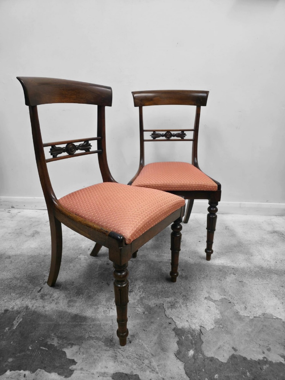 A pair of antique mahogany dining chairs featuring curved top rails, carved central back splats, turned front legs, and peach fabric upholstered seats.