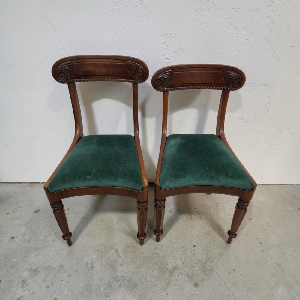 A pair of antique Regency mahogany dining chairs featuring curved carved crest rails and green velvet upholstered seats.