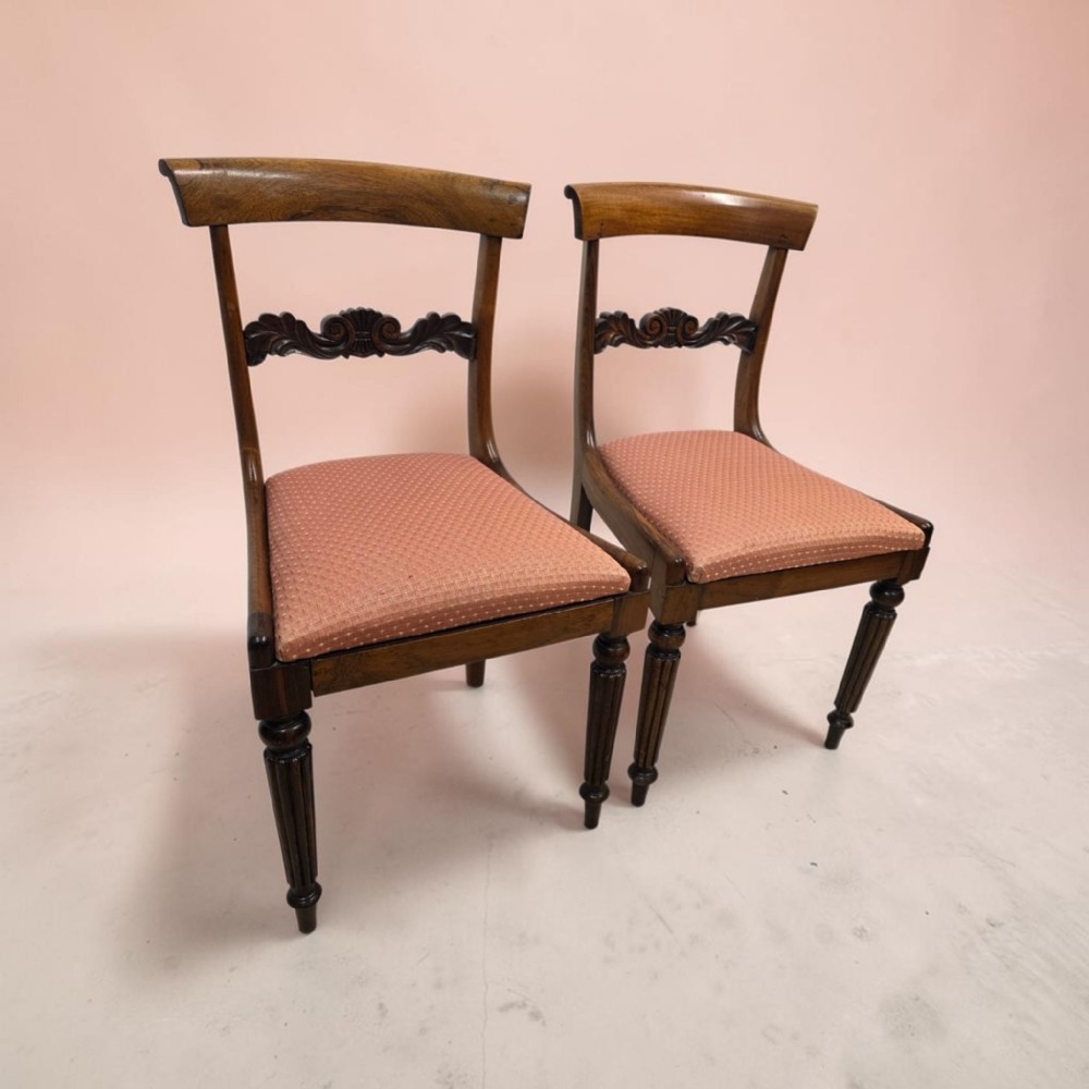 A pair of late Regency mahogany dining chairs featuring carved back rails, turned fluted legs, and patterned rose pink upholstered seats.