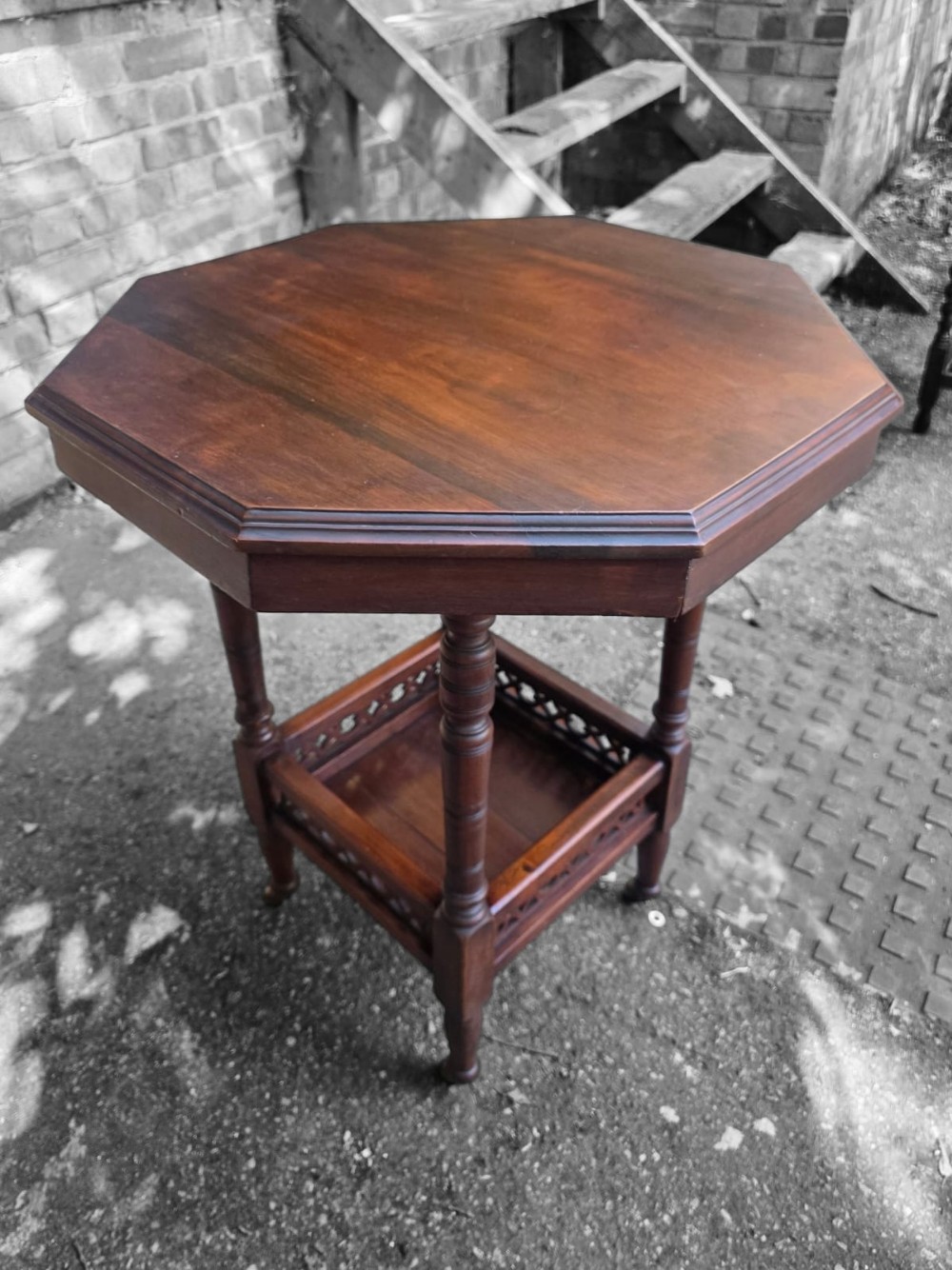 A late Victorian octagonal wooden side table featuring turned legs and a square lower shelf with pierced fretwork sides.
