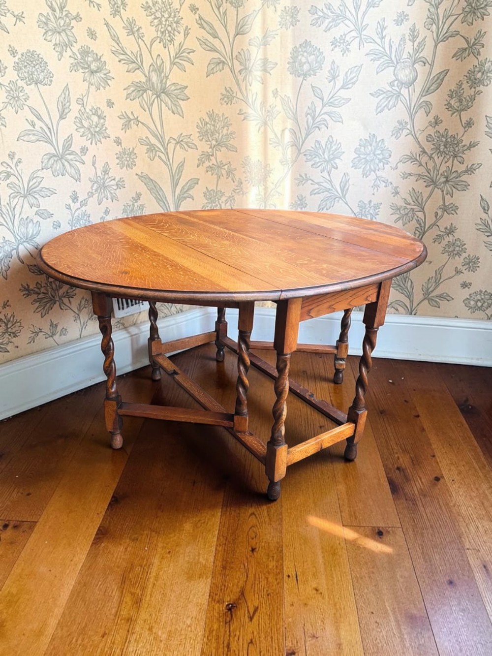 An antique oak gateleg dining table featuring a rounded drop-leaf top supported by turned barley twist legs and lower stretchers.