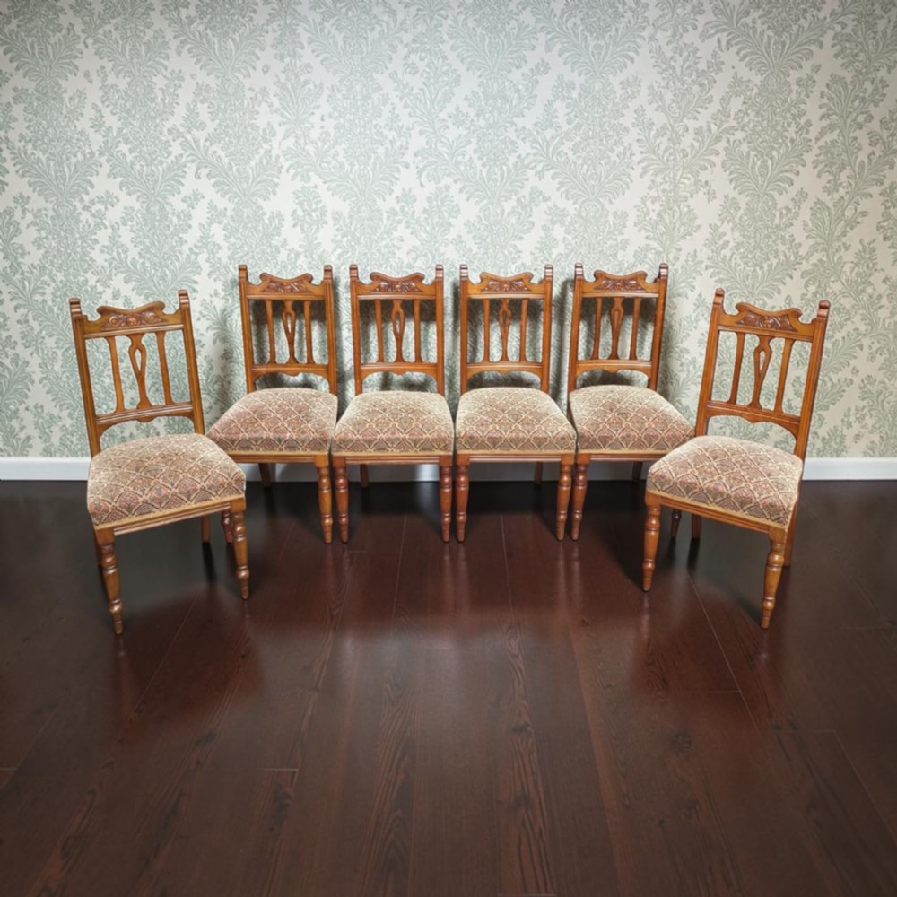 A set of six Edwardian oak dining chairs featuring carved cresting rails, vertical splat backs, turned front legs, and patterned fabric seats.