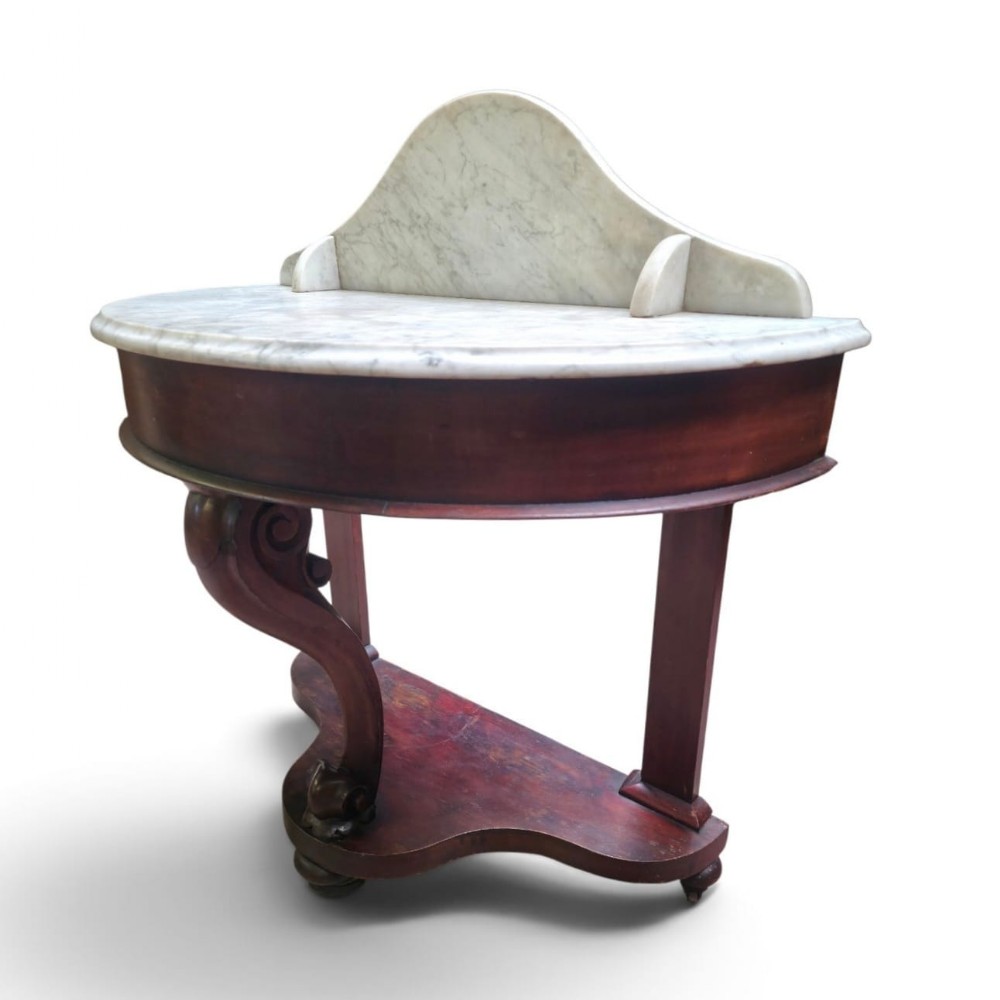 A Victorian mahogany washstand featuring a curved white marble top with a splashback and a single carved scroll front leg.