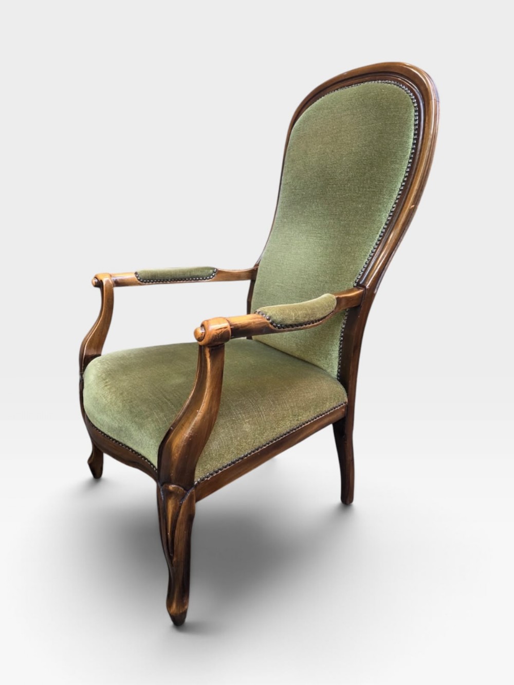 An antique Victorian high back armchair featuring a polished timber frame, olive green velvet upholstery, and brass stud trim.