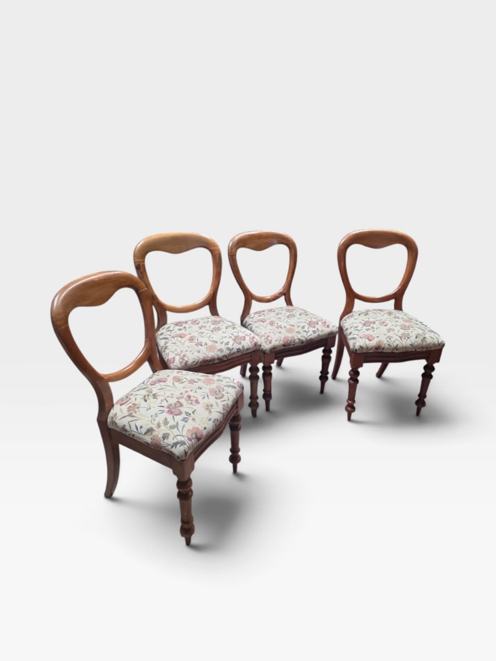 Set of four Victorian mahogany dining chairs featuring open rounded balloon backrests, turned front legs, and floral fabric upholstered seats.