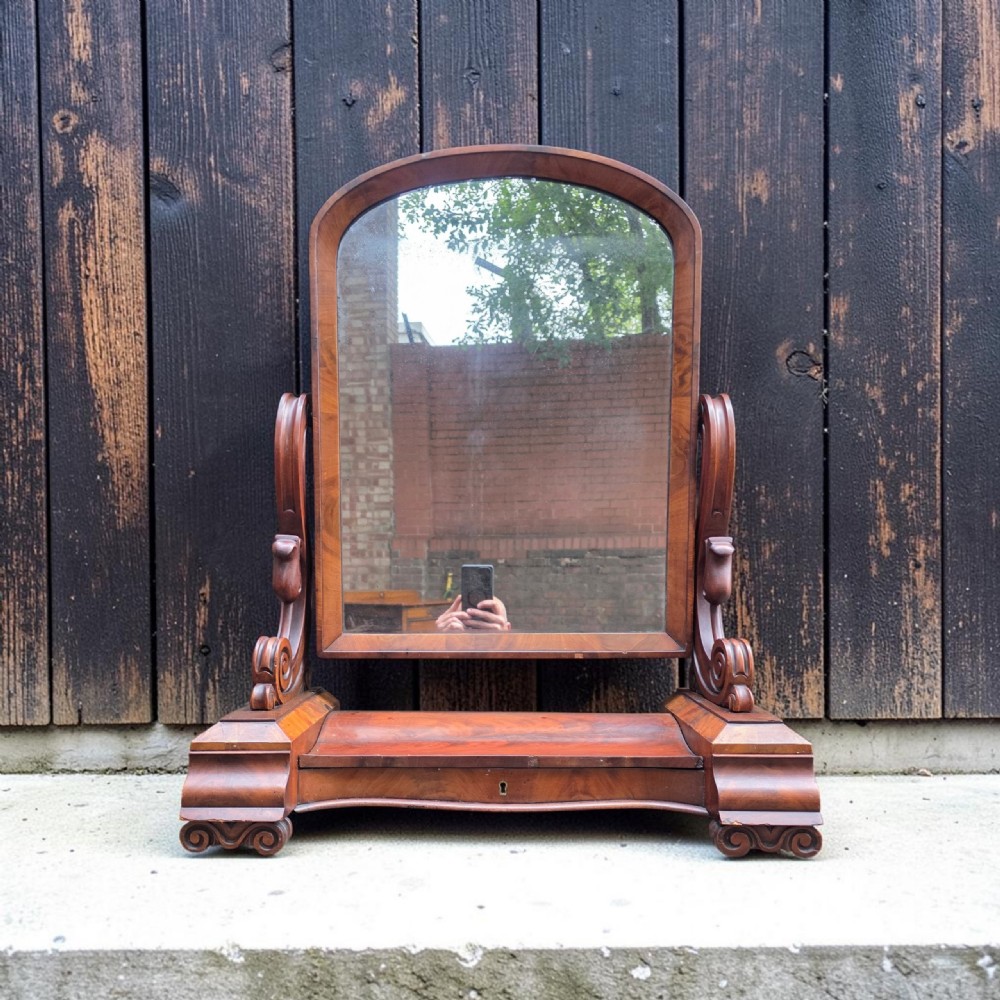 A William IV mahogany dressing table mirror featuring an arched frame, carved scroll supports, and a shaped plinth base.