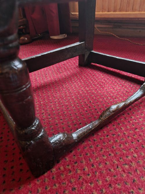 fig 1. A seventeenth-century dark oak wainscot armchair featuring a solid panelled backrest, carved top rail, curved armrests, and turned leg supports.