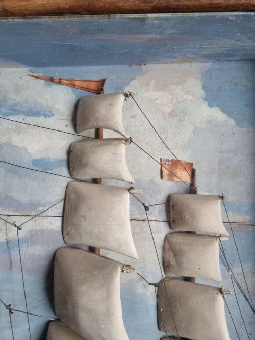 fig 1. A framed three-dimensional naive wooden diorama depicting a multi-masted sailing ship on a painted sea against a cloudy sky background.