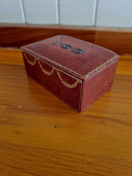 fig 1. A small rectangular deep red Morocco leather stamp box with gilt festoon decoration and applied metal initials on the lid.