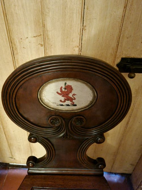 fig 1. A Regency mahogany hall chair featuring an oval back panel with a central painted heraldic crest, a solid timber seat, and turned front legs.