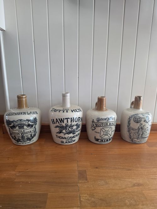 fig 1. A set of four 19th-century cream stoneware advertising whisky flasks featuring black transfer-printed text and brown glazed spouts.