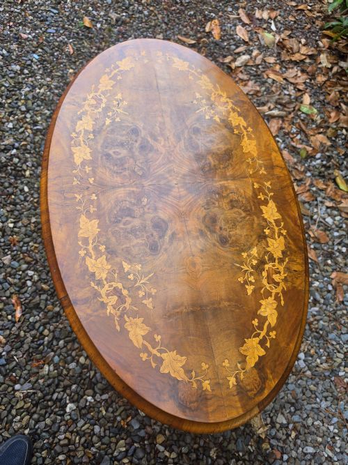 fig 1. An oval 19th-century burr walnut centre table featuring floral marquetry inlay, supported by turned central columns and four carved legs.