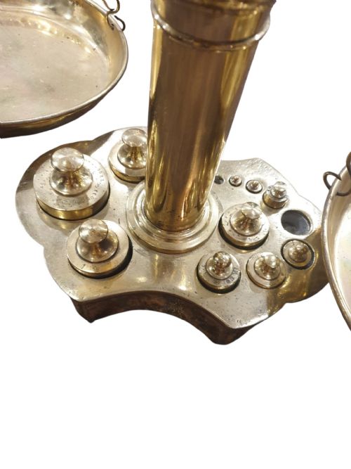 fig 1. A large polished brass balance scale featuring a central column topped with a sculpted bull head finial and multiple hanging circular brass pans.
