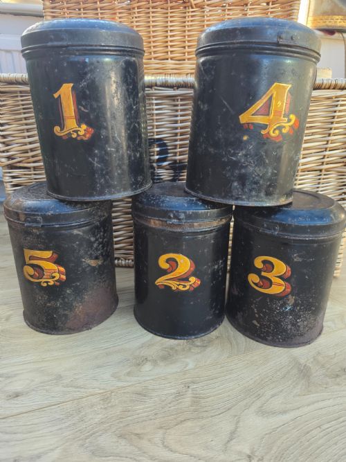 fig 1. A set of five cylindrical black tin tea canisters numbered one through five with ornate gold and red painted numerals.