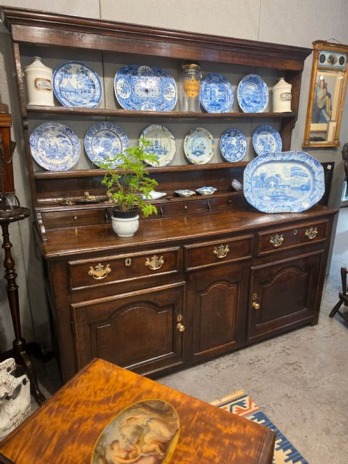fig 1. An 18th-century dark oak Welsh dresser featuring a three-tiered plate rack top above three drawers and three panelled cupboard doors with brass handles.