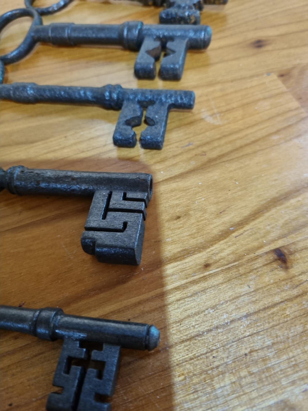 A set of six antique dark cast iron keys with rounded bows and notched bits lying in a row. View II