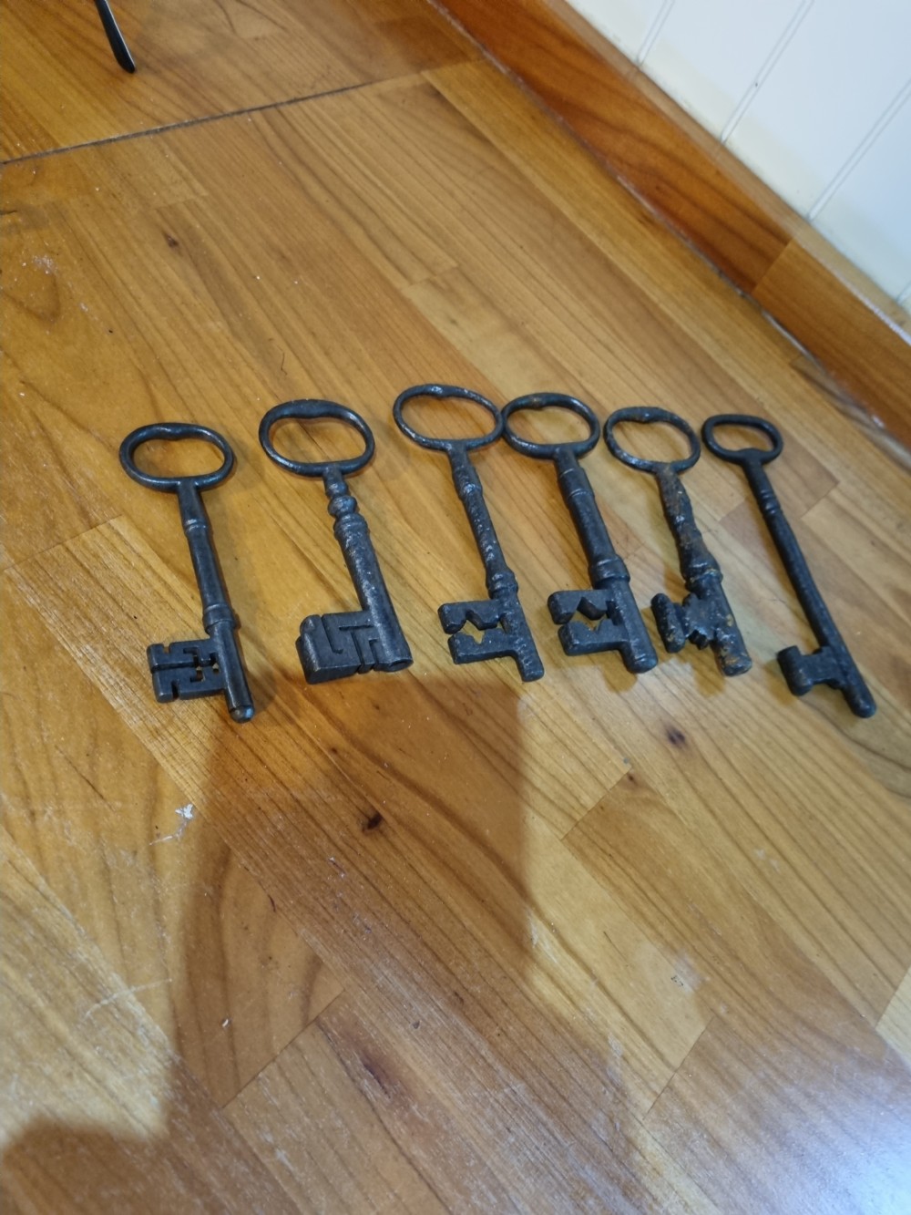 A set of six antique dark cast iron keys with rounded bows and notched bits lying in a row. View V