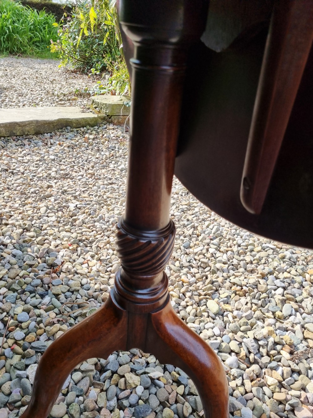 An antique Georgian circular mahogany tripod table shown tilted vertically on a turned stem with three cabriole legs. View II