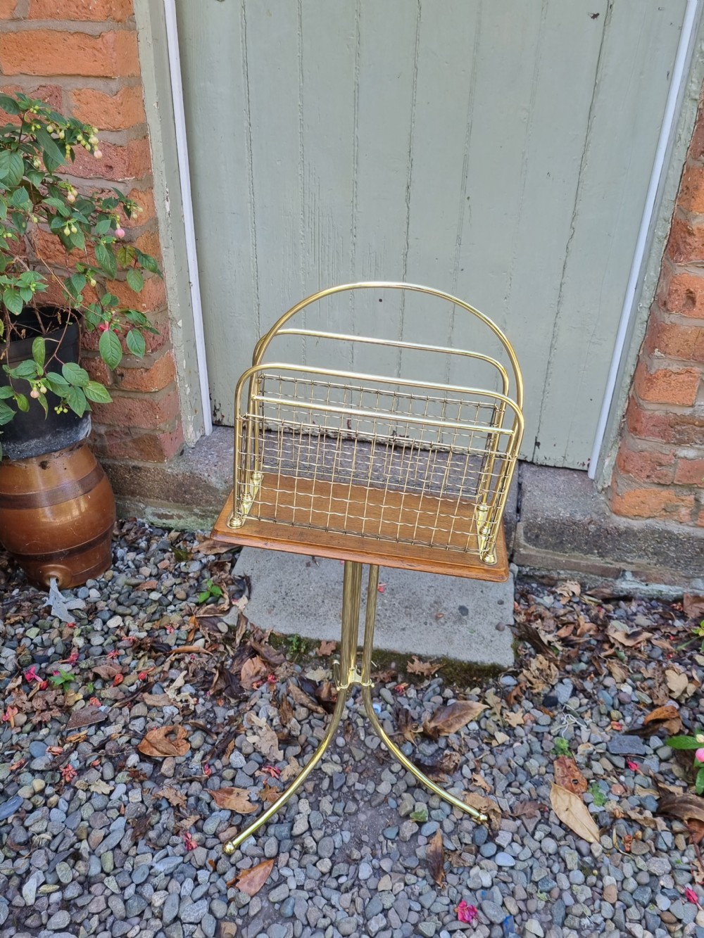 A tall standing brass magazine rack featuring a wire mesh basket, a polished mahogany base, and a three-legged brass tripod stand. View III