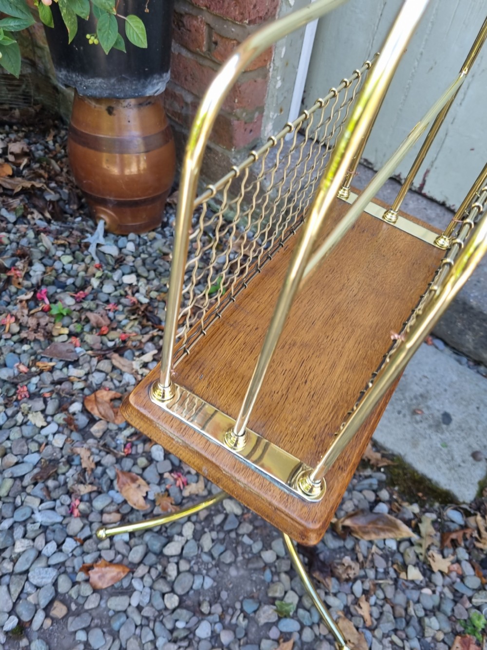 A tall standing brass magazine rack featuring a wire mesh basket, a polished mahogany base, and a three-legged brass tripod stand. View V