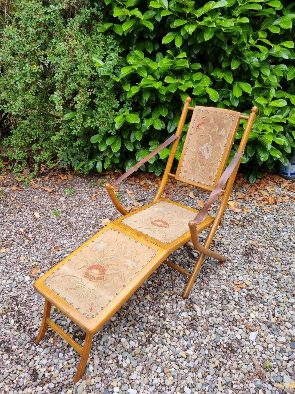 A 19th-century light oak folding lounge chair with floral tapestry panels, leather strap armrests, and an extended footrest. View II
