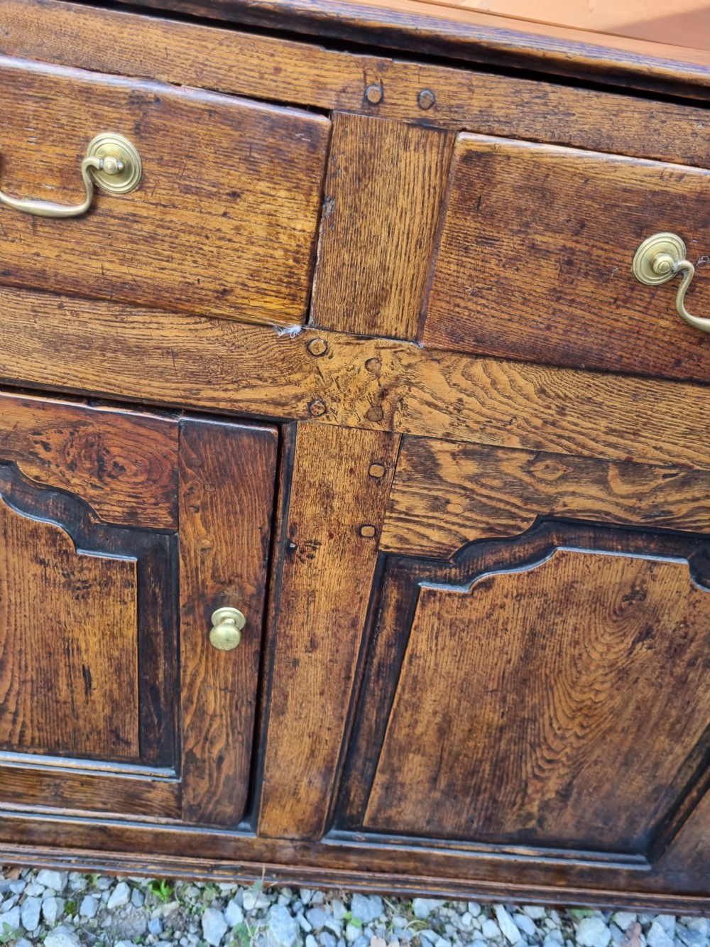 A mid-18th century dark oak dresser base featuring three top drawers over three fielded panel cupboard doors with brass swan neck handles. View V