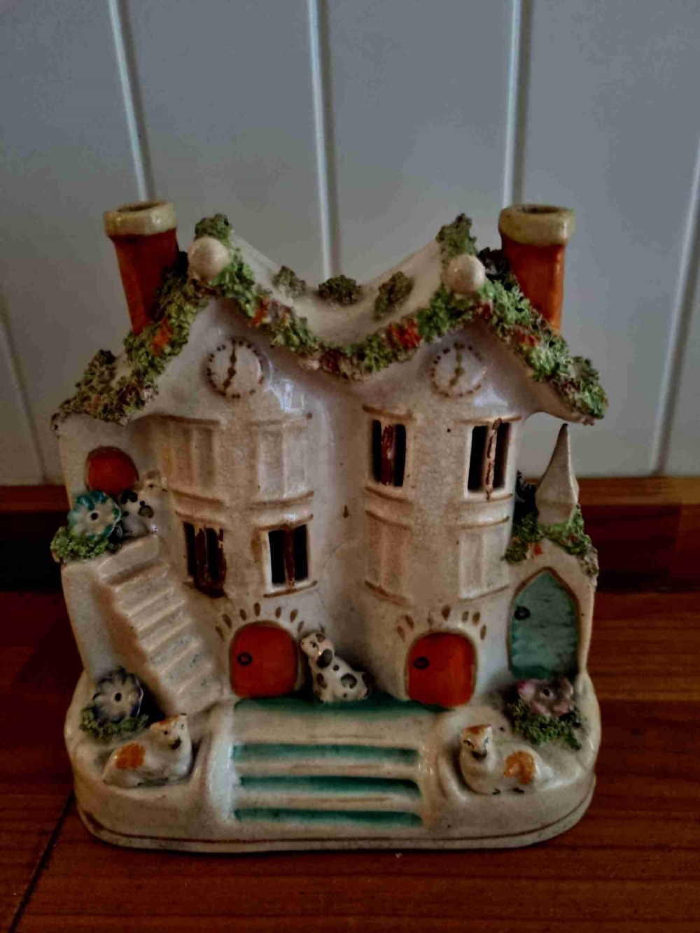 A 19th-century Staffordshire earthenware pastille burner styled as a cream twin-gabled mansion with applied green foliage and painted red doors.