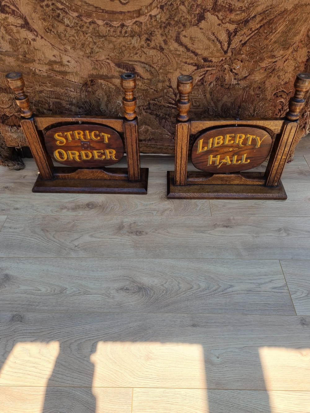 A pair of carved dark oak tabletop signs with oval central plaques featuring painted gold lettering reading Liberty Hall and Strict Order. View V