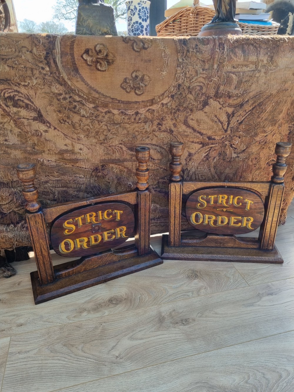 A pair of carved dark oak tabletop signs with oval central plaques featuring painted gold lettering reading Liberty Hall and Strict Order. View VII