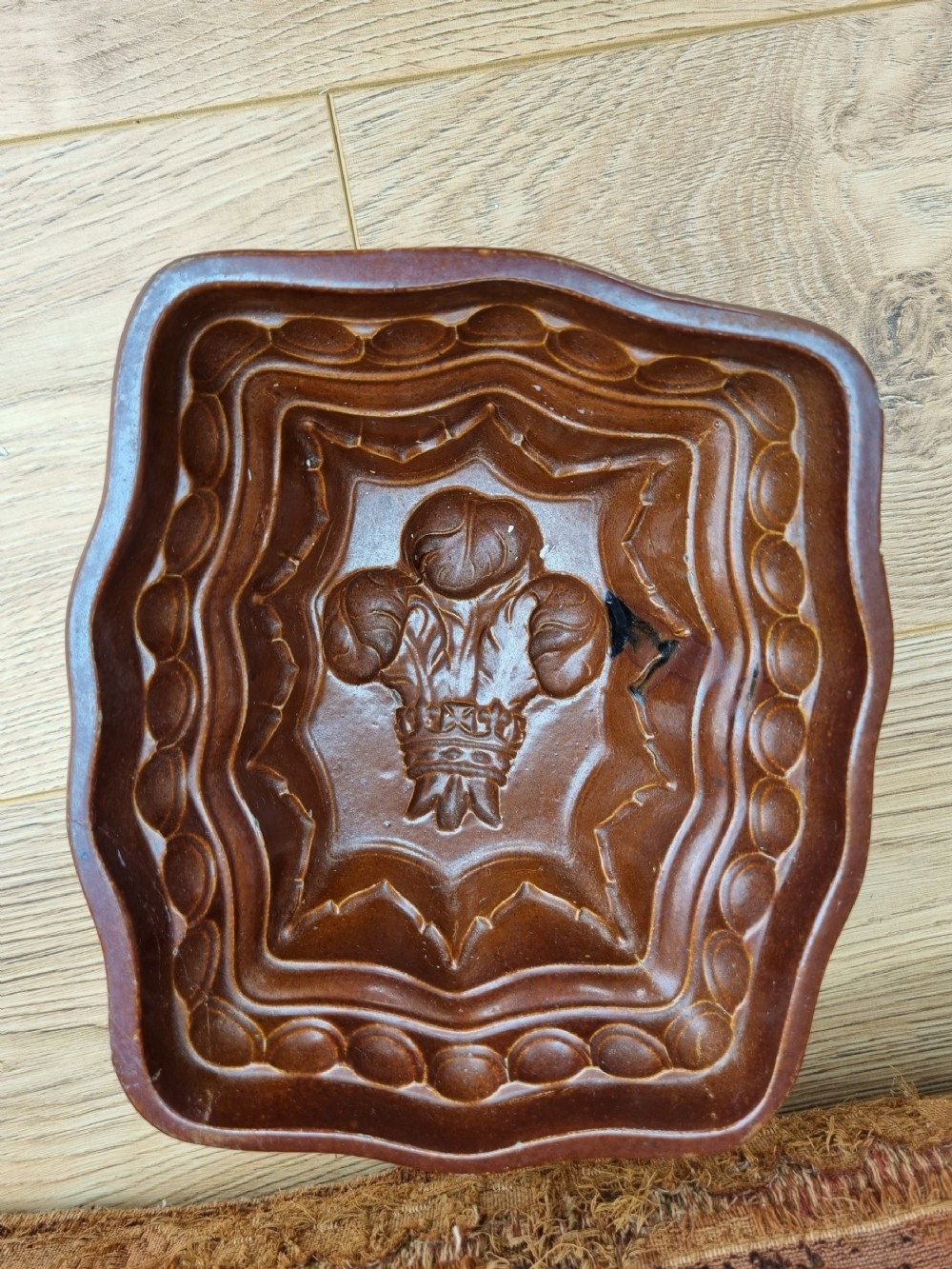 A square brown glazed stoneware jelly mould with a central Prince of Wales feathers relief motif and stepped fluted sides.
