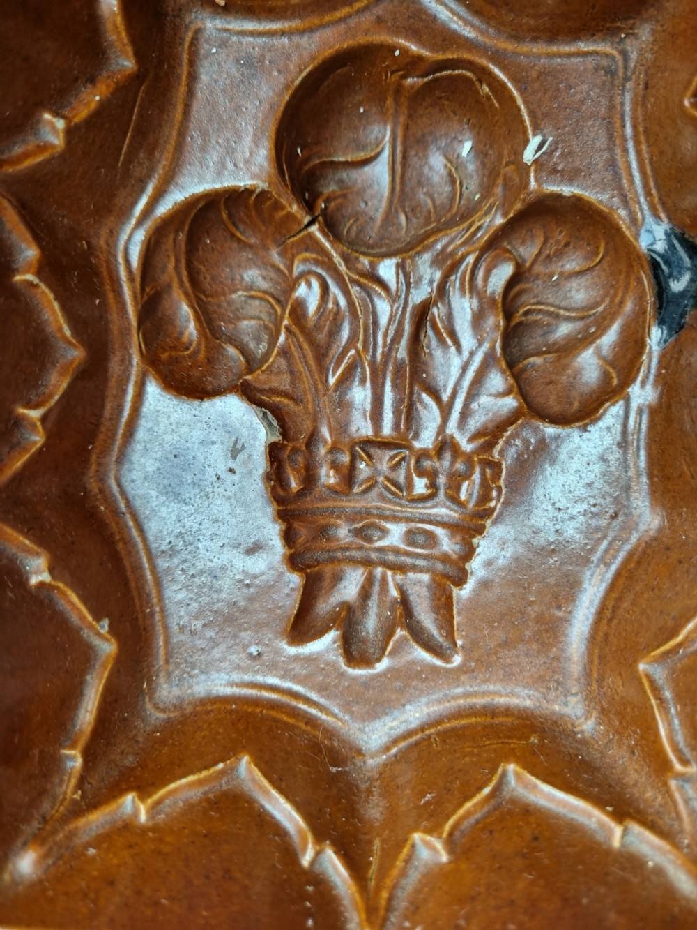 A square brown glazed stoneware jelly mould with a central Prince of Wales feathers relief motif and stepped fluted sides. View II