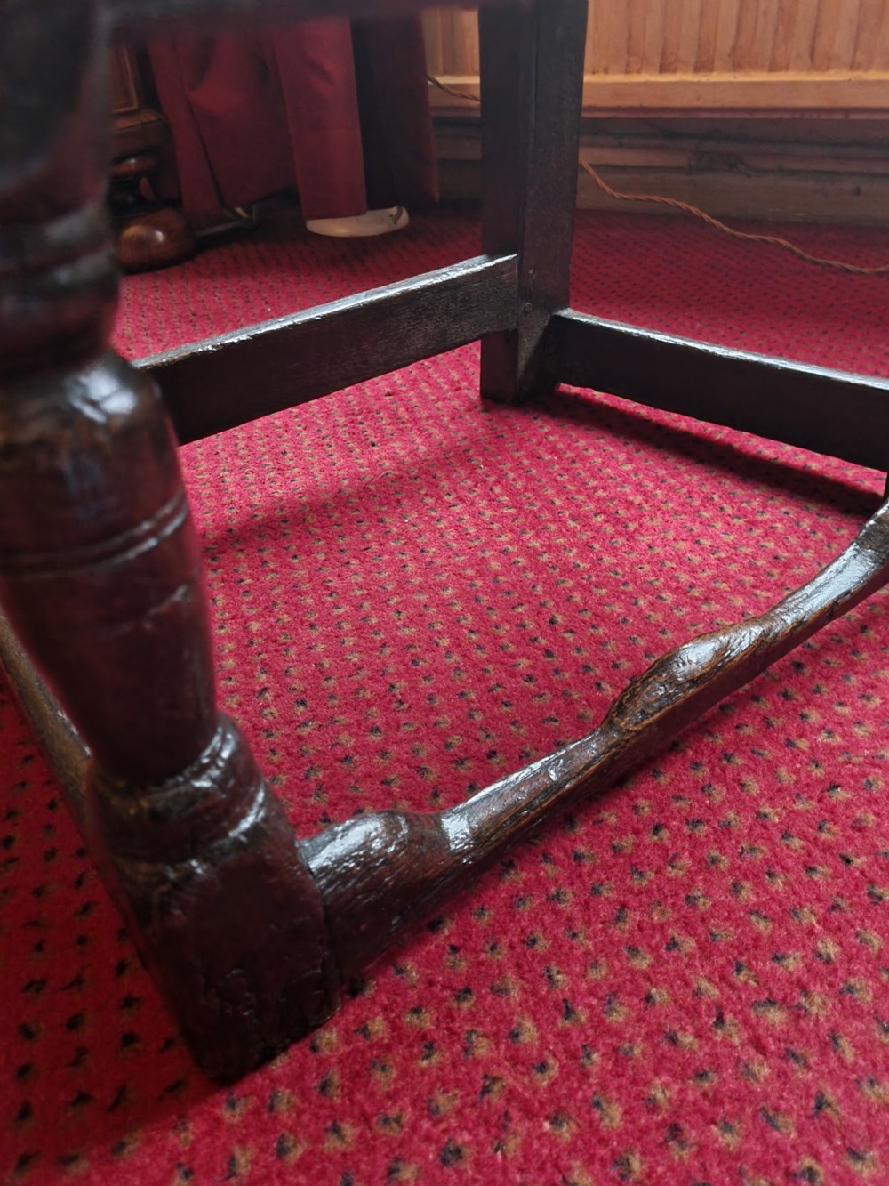A seventeenth-century dark oak wainscot armchair featuring a solid panelled backrest, carved top rail, curved armrests, and turned leg supports. View II