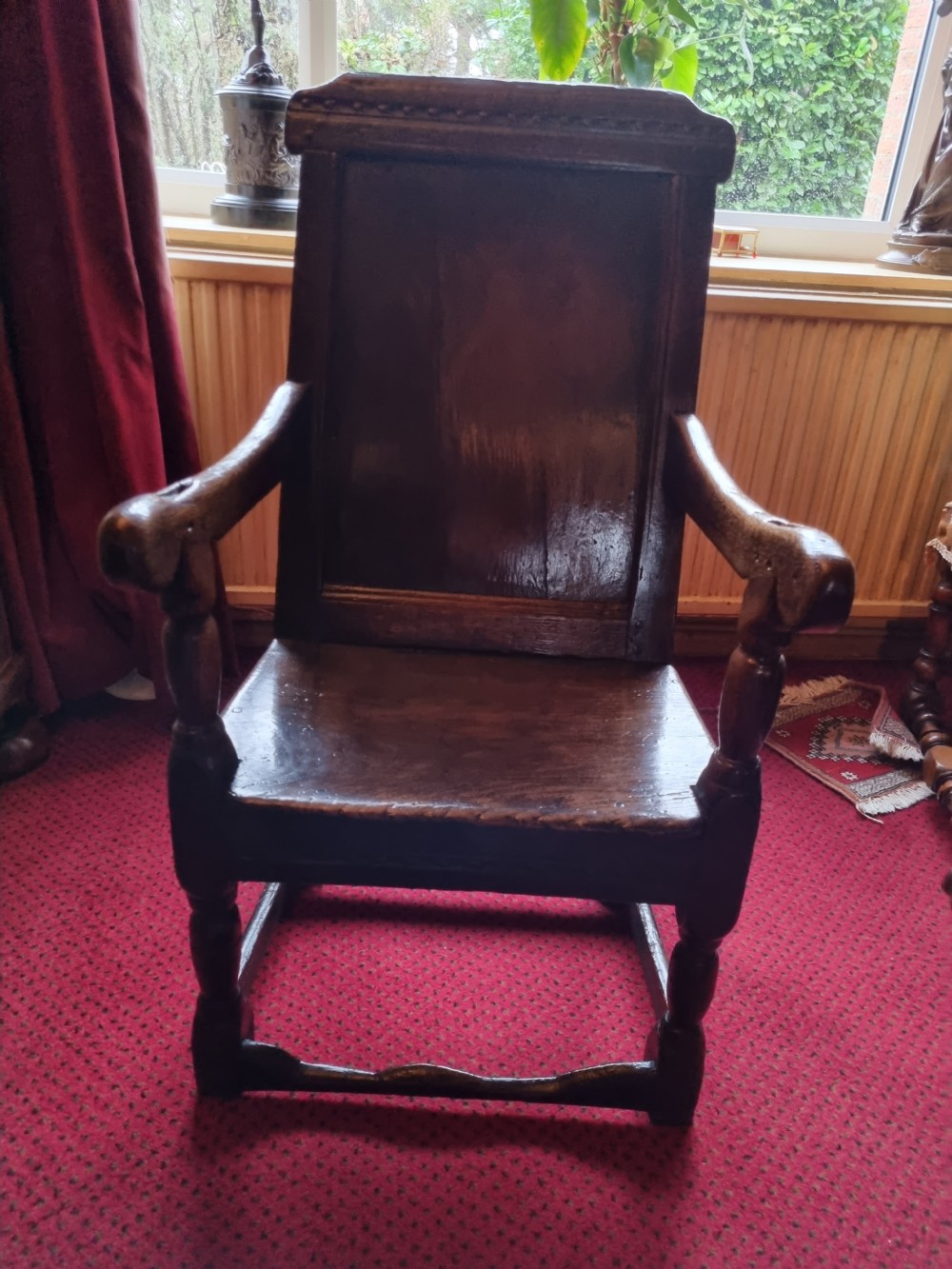 A seventeenth-century dark oak wainscot armchair featuring a solid panelled backrest, carved top rail, curved armrests, and turned leg supports. View III