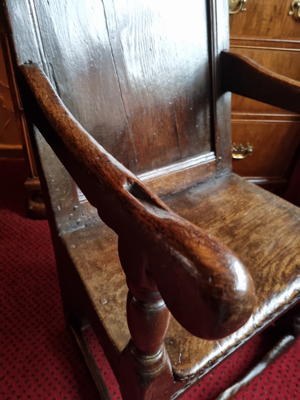 A seventeenth-century dark oak wainscot armchair featuring a solid panelled backrest, carved top rail, curved armrests, and turned leg supports. View IV