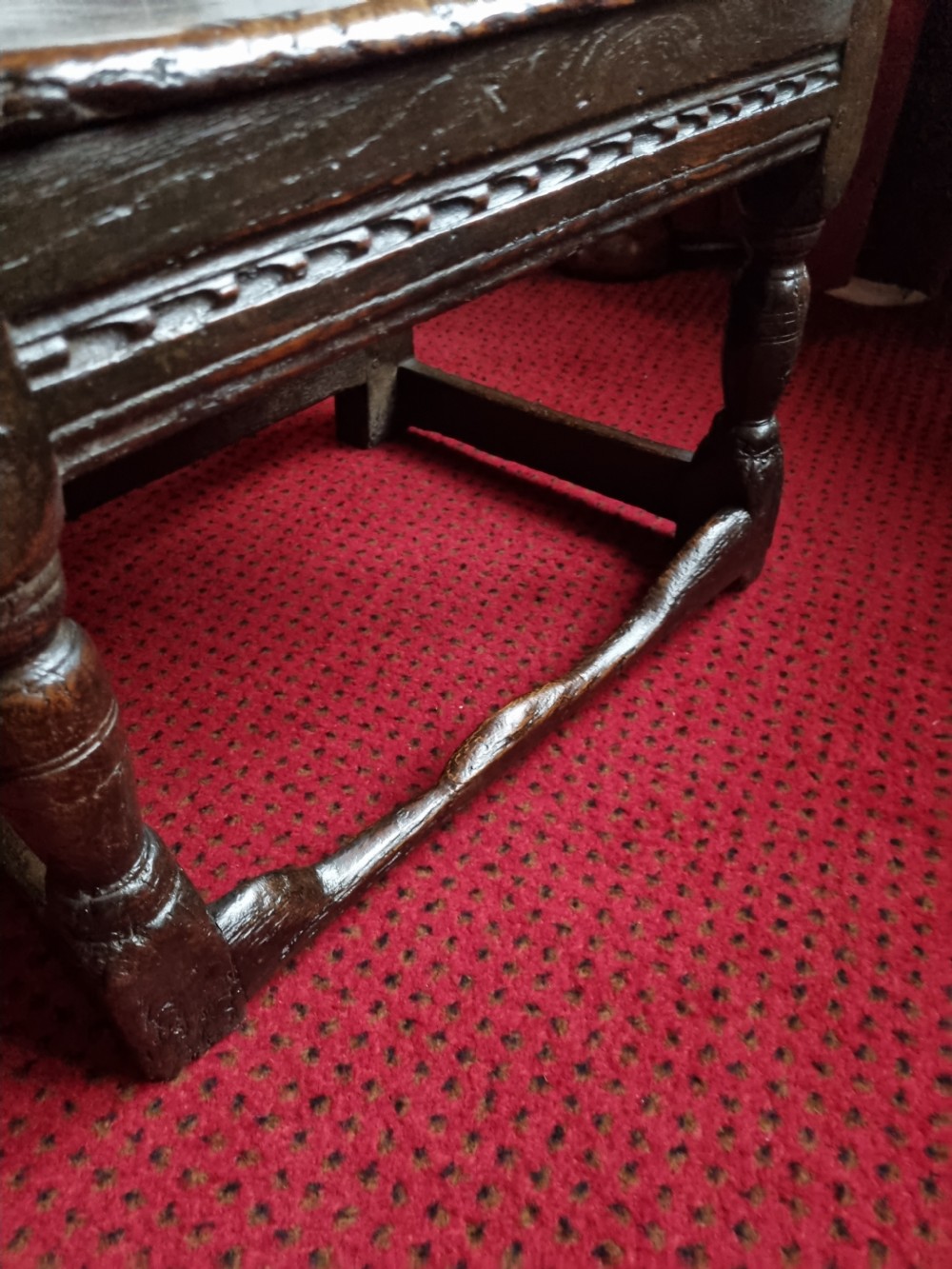 A seventeenth-century dark oak wainscot armchair featuring a solid panelled backrest, carved top rail, curved armrests, and turned leg supports. View V