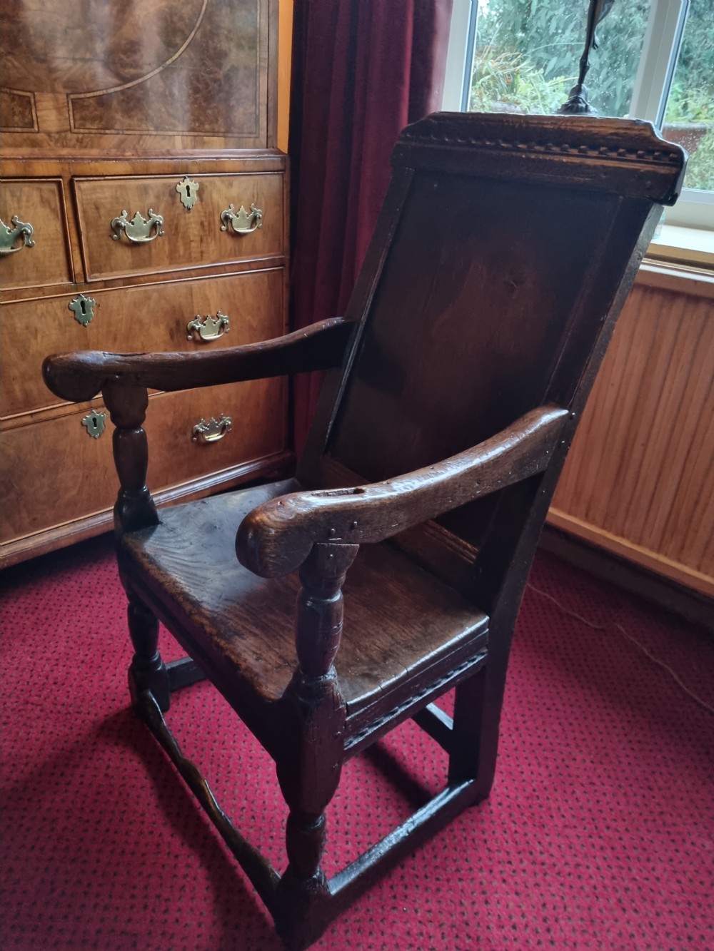 A seventeenth-century dark oak wainscot armchair featuring a solid panelled backrest, carved top rail, curved armrests, and turned leg supports. View VII