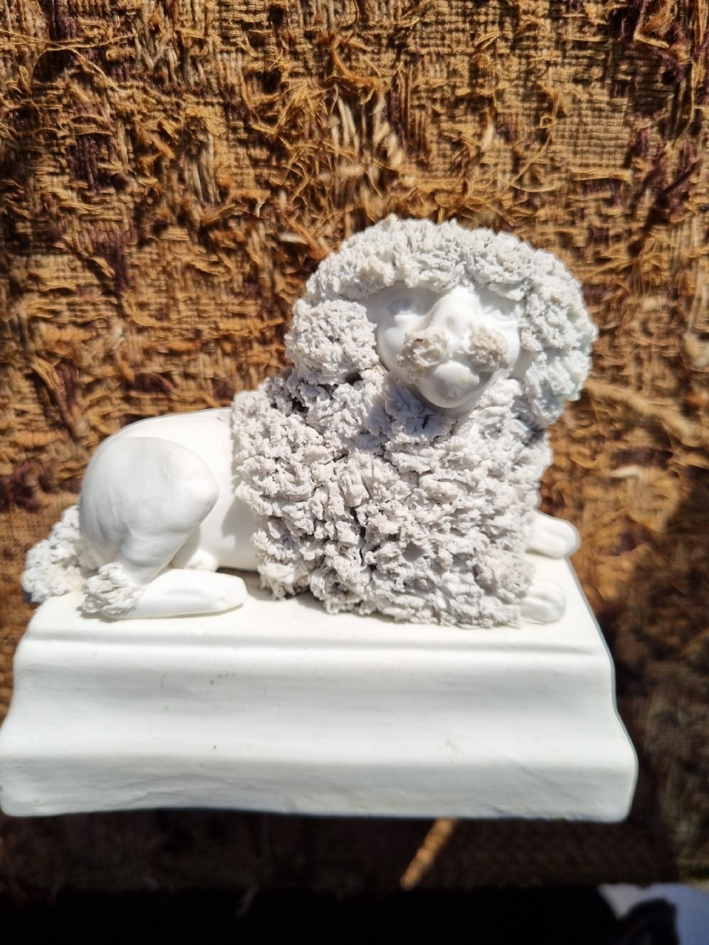An early 19th-century off-white bisque porcelain figurine of a recumbent poodle with texturized ceramic fur resting on a rectangular stepped base.