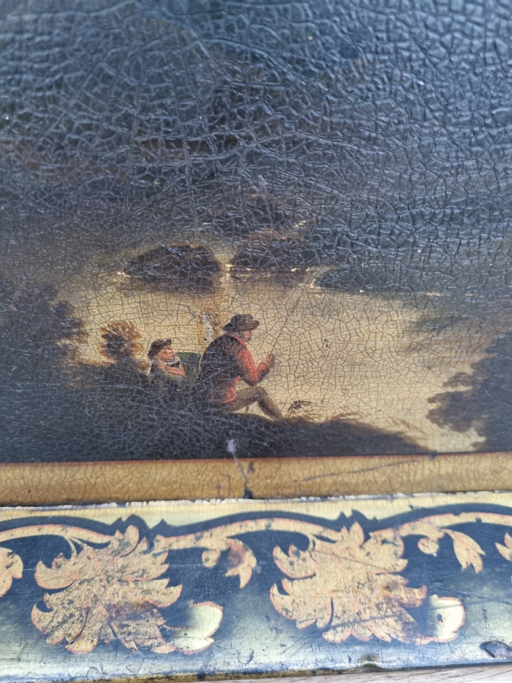 An 18th-century rectangular papier-mache tray featuring a painted landscape scene with figures fishing and a gilded foliate border. View II