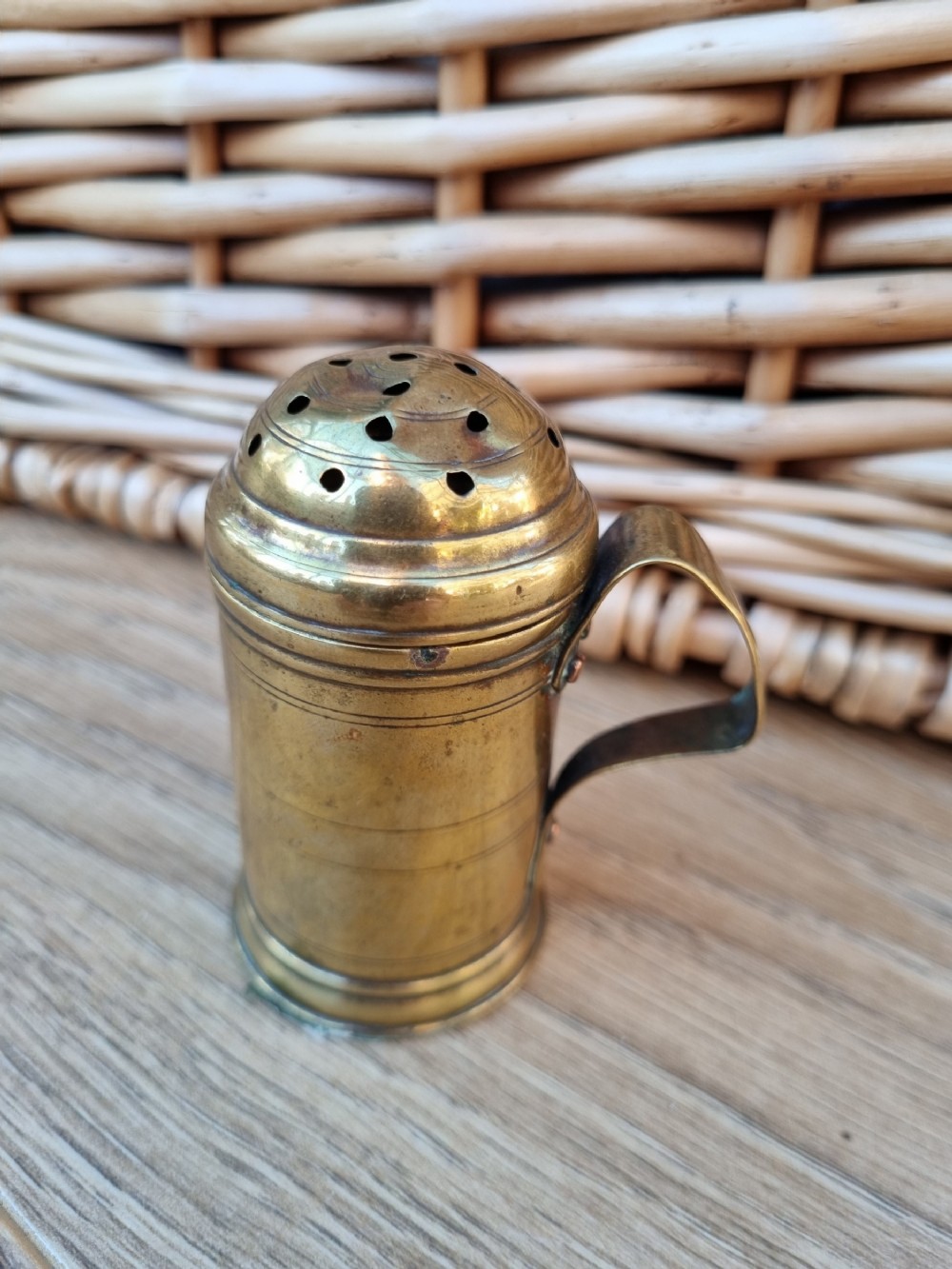 A 19th-century cylindrical brass sugar sifter featuring a perforated domed lid, incised line detailing, and a curved strap handle.