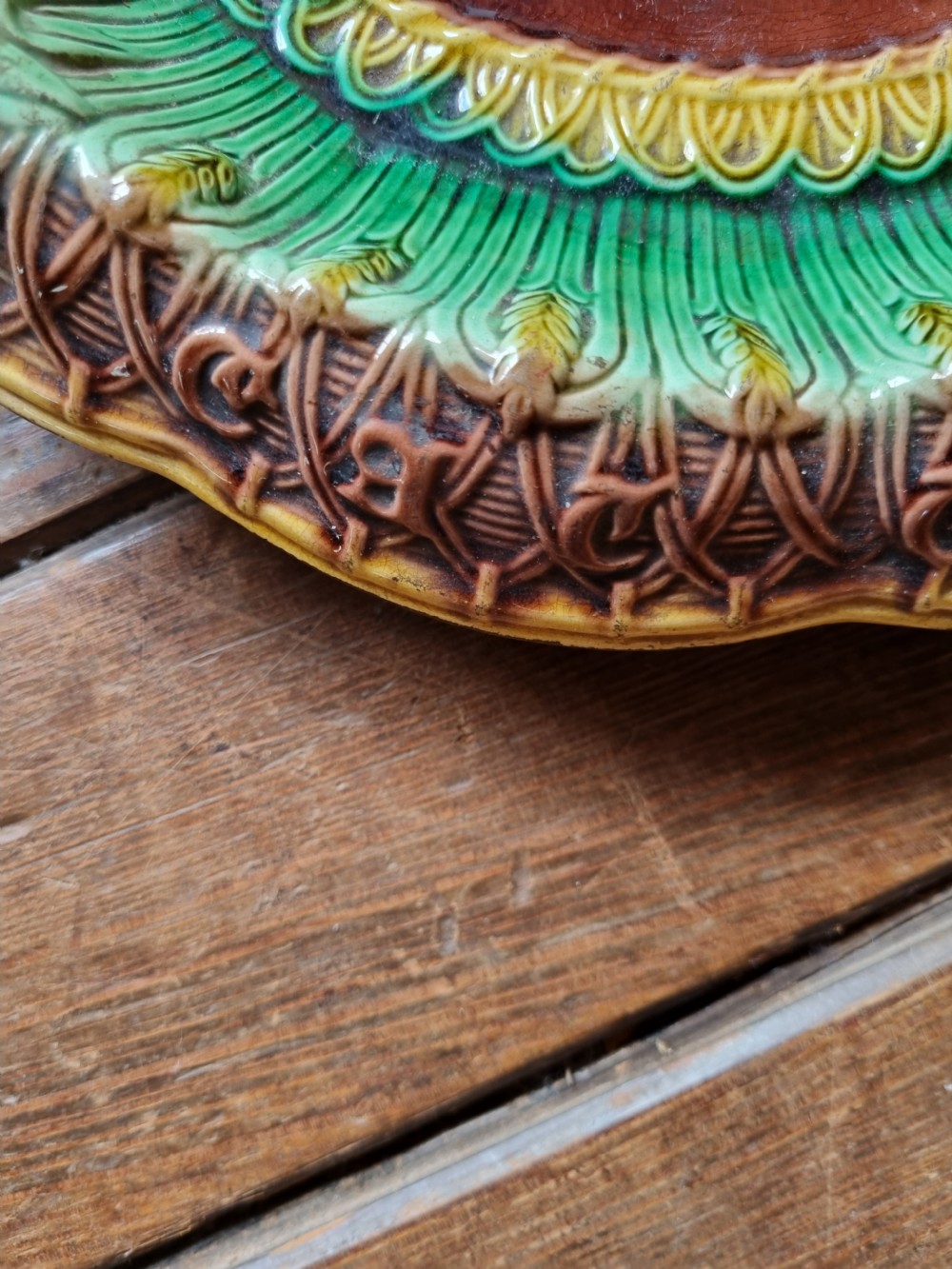 An oval Victorian majolica earthenware bread plate featuring a brown central field surrounded by moulded green and yellow wheat motifs. View V