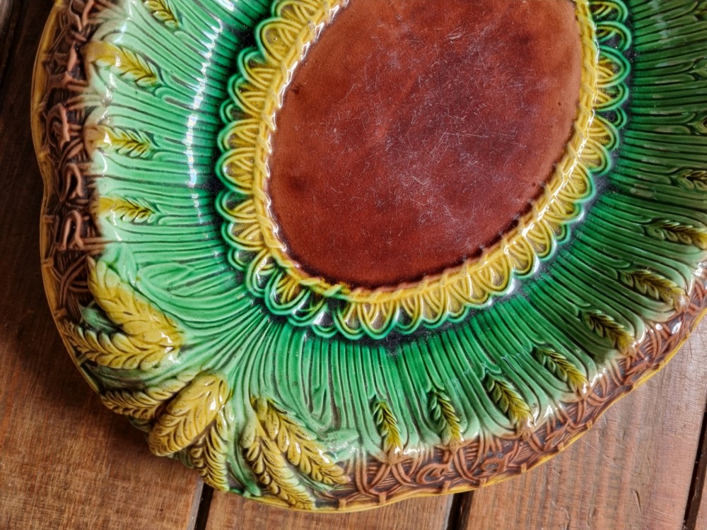 An oval Victorian majolica earthenware bread plate featuring a brown central field surrounded by moulded green and yellow wheat motifs. View VI