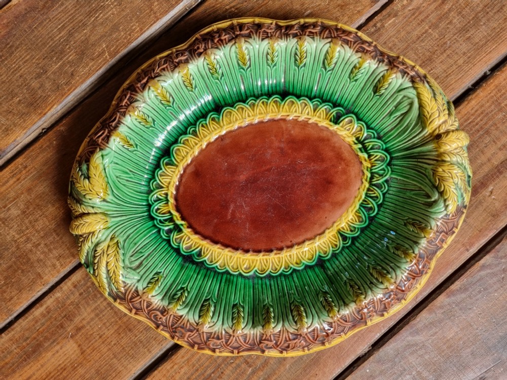 An oval Victorian majolica earthenware bread plate featuring a brown central field surrounded by moulded green and yellow wheat motifs. View VII