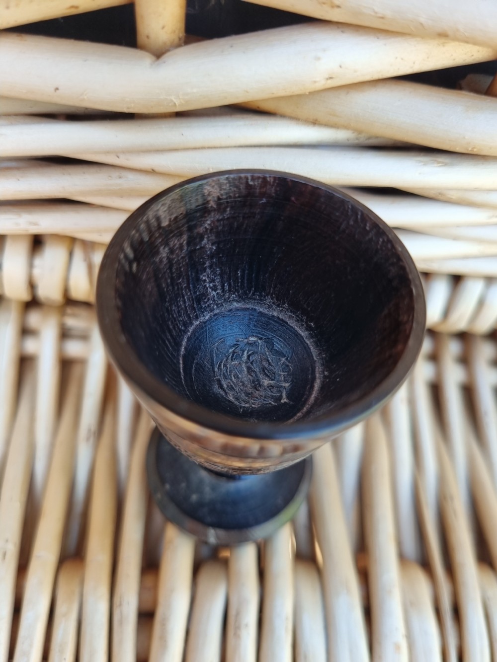 A small turned solid ebony goblet featuring a rounded bowl and a stepped foot base, set against a wicker background. View III