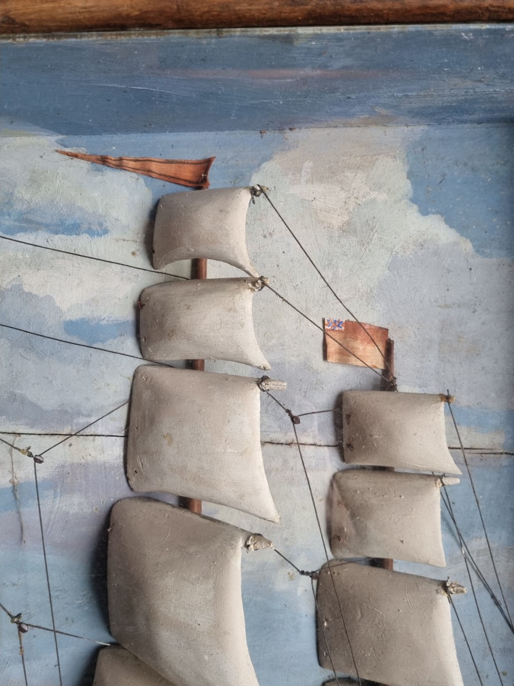 A framed three-dimensional naive wooden diorama depicting a multi-masted sailing ship on a painted sea against a cloudy sky background. View II