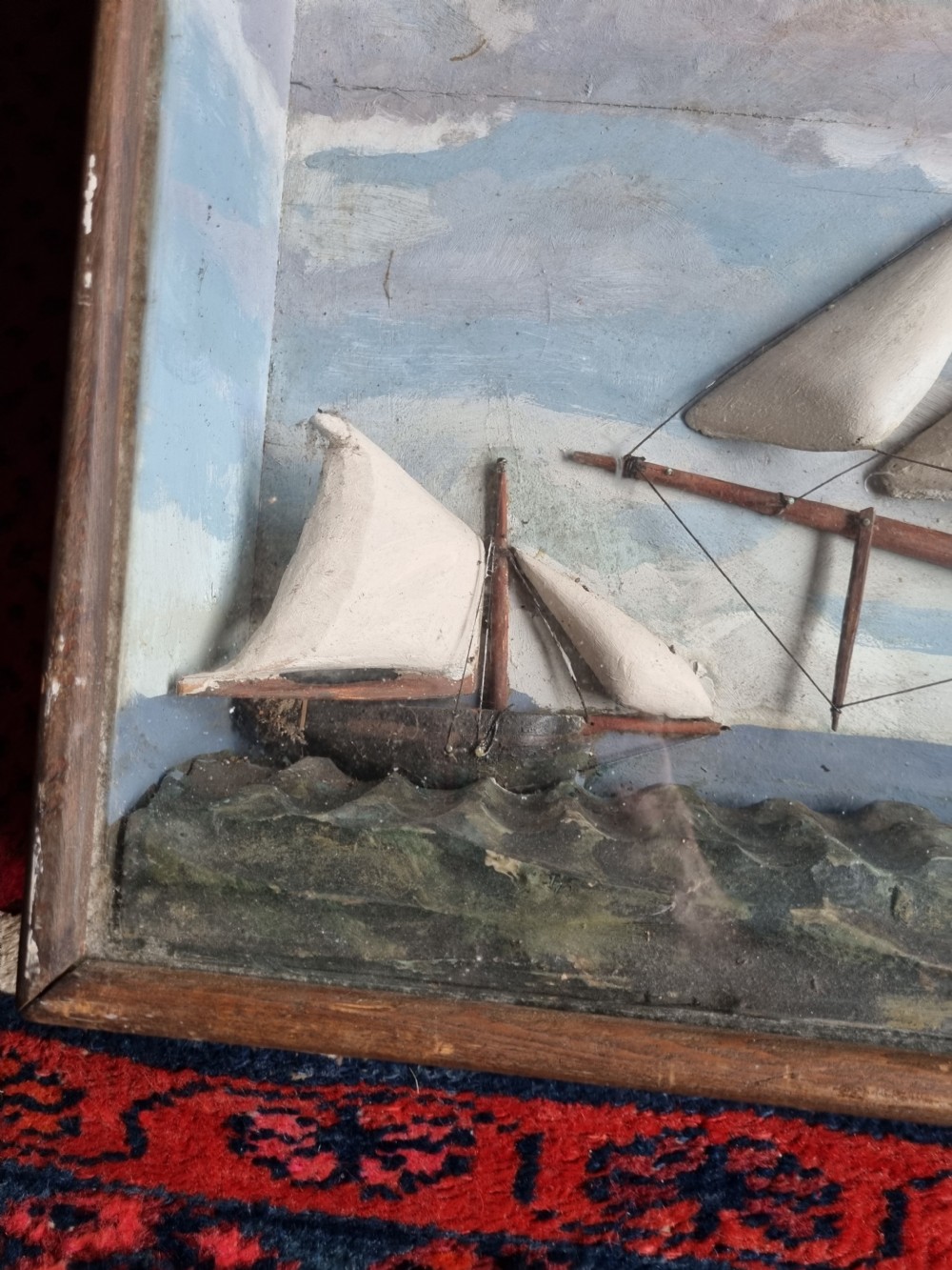 A framed three-dimensional naive wooden diorama depicting a multi-masted sailing ship on a painted sea against a cloudy sky background. View V