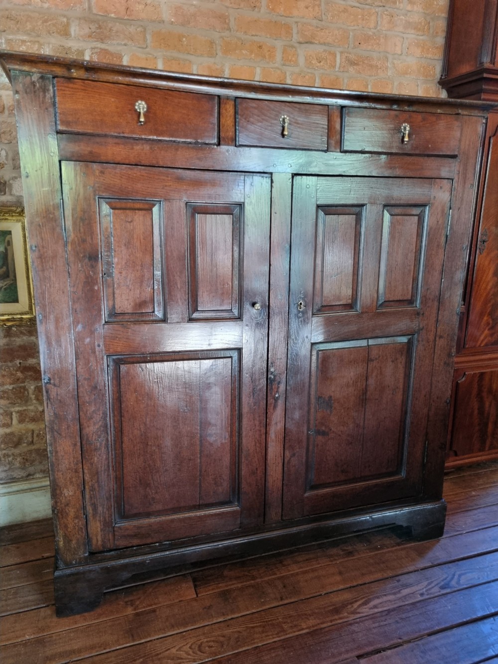 An 18th-century dark oak Welsh hanging cupboard featuring three upper drawers above double raised-panel doors. View VII