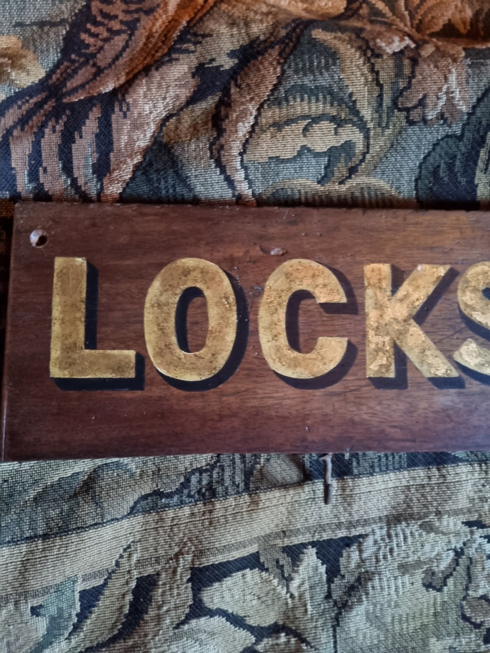 A rectangular dark oak board featuring raised gold lettering spelling the word LOCKSMITH. View II