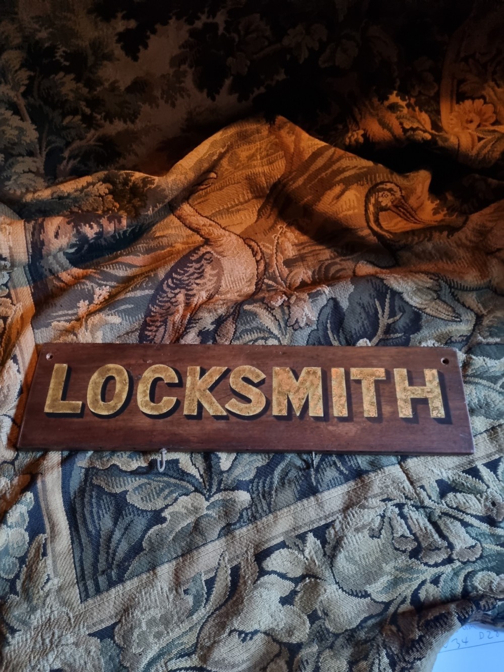 A rectangular dark oak board featuring raised gold lettering spelling the word LOCKSMITH. View V
